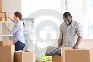 Interracial couple unpacking boxes indoors. Moving into new house