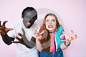 Interracial couple wearing casual clothes shouting frustrated with rage, hands trying to strangle, yelling mad