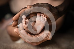 Interracial family holding baby feet in hands mixed by black and white skin color