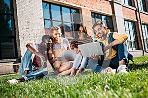 interracial group of students with laptops and notebooks studying on green