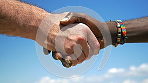 Interracial handshake on sky background