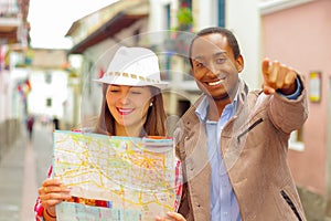 Interracial happy couple wearing casual clothes in urban envrionment, interacting and looking at map