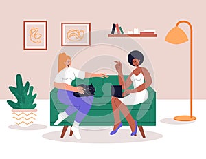 Interracial lesbian couple relaxing on comfy sofa in living room. Spending time together in apartment. Woman with laptop