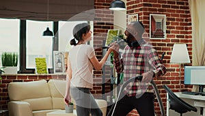 Interracial partners having fun cleaning room with vacuum cleaner and mop