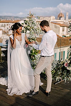 Interracial wedding couple. Destination fine-art wedding in Florence, Italy. A wedding ceremony on the roof of the