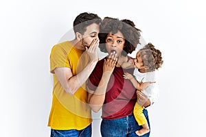 Interracial young family of black mother and hispanic father with daughter hand on mouth telling secret rumor, whispering