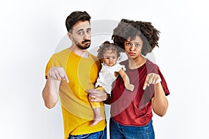 Interracial young family of black mother and hispanic father with daughter pointing down looking sad and upset, indicating