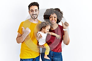 Interracial young family of black mother and hispanic father with daughter pointing to the back behind with hand and thumbs up,