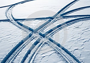 Intersecting tire tracks in smooth, white snow form a noticeable pattern