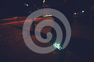 intersection at night with traffic light for a cycling lane showing green bicycle symbol and moving lights in blurred background