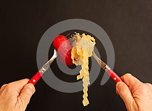 An intersection of two forks with noodles and tomato