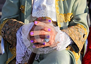 intertwined hands of people with purple malt nails and noble clothes