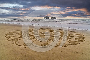 Intricate mandala sand art on a beach.