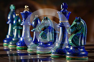 Intricately designed cobalt blue and emerald green chess set on reflective surface, symbolizing strategy and competition