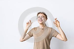 Young woman in t-shirt praying with crossed fingers and looking away over grey background