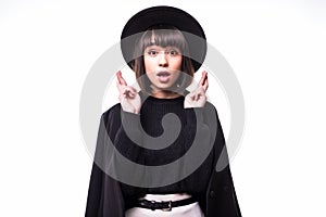 Intrigued young woman praying with crossed fingers and looking away over white background