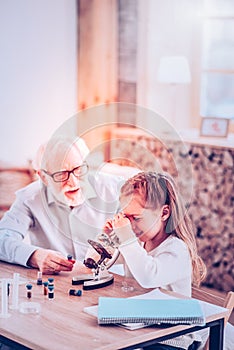 Intriguing girl considering microelement in microscope at home