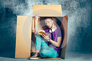 Introvert concept. Man sitting inside box and reading book