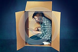 Introvert concept. Woman sitting inside box and working with laptop