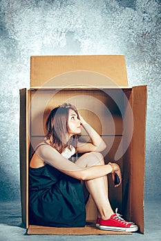 Introvert concept. Woman sitting inside box and working with phone