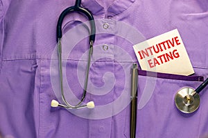 Intuitive eating symbol. Medical uniform, white card with words Intuitive eating, metalic pen and stethoscope. Medical and