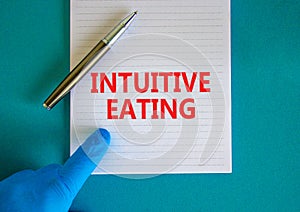 Intuitive eating symbol. White note with words Intuitive eating, beautiful blue background, doctor hand and metallic pen. Medical