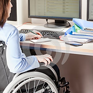 Invalid or disabled woman sitting wheelchair working office desk computer photo