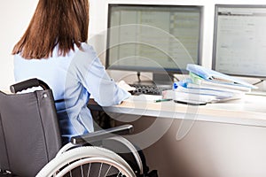 Invalid or disabled woman sitting wheelchair working office desk computer photo