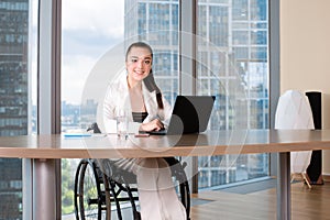 Invalid or disabled young business woman person sitting wheelchair working in office on a laptop