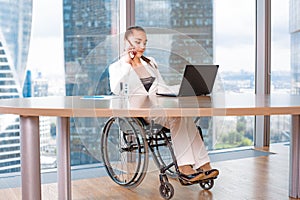 Invalid or disabled young business woman person sitting wheelchair working in office on a laptop