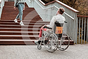 Invalid man sitting in the wheelchair and looking at the stairs