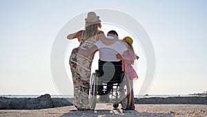 Invalid people in backlight, daddy in wheelchair hugging daughter on background blue sky, disabled man