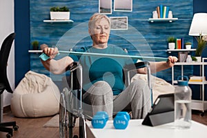 Invalid senior woman exercising arm muscle resistance using elastic band watching fitness video