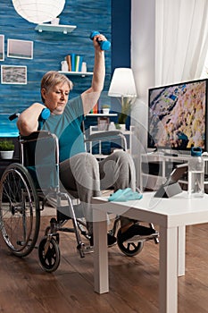 Invalid senior woman holding workout dumbbells raising arm while exercising body muscle
