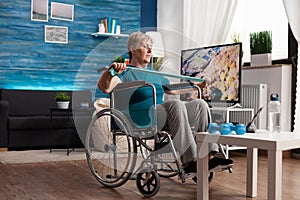 Invalid senior woman in wheelchair holding resistance elastic band stretching body muscle