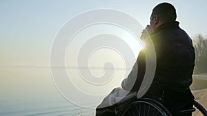 Invalid on wheelchair, disabled person, cup of warming drink in hands of crippled Man handicapped Man meets dawn with
