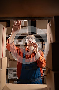 Inventory manager using headset in distribution warehouse searching packages on shelf.