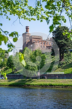 Inverness Castle with tree leaves and river in front, Scotland, vertical shot