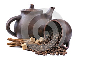 Inverted mug with coffee beans on the background of a clay teapot, isolated on white