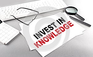 INVEST IN KNOWLEDGE text on a paper on a gray background near a calculator and a white keyboard