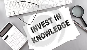 INVEST IN KNOWLEDGE text on paper with keyboard, calculator on grey background