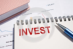 INVEST text written on notepad with pen on financial documents