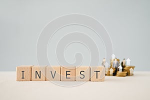 INVEST word on wooden cube blocks with blurred stack of coin and businessman miniature. For Financial investment growth or