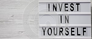 `Invest in yourself` words on a modern board over white wooden background, top view. Overhead, flat lay, from above. Copy space