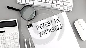 INVEST IN YOURSELF written on paper with office tools and keyboard on the grey background