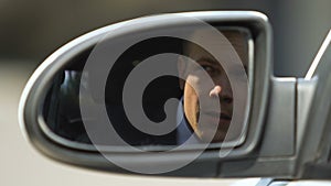 Investigating businessman looking outside car, rear mirror view, suspicion