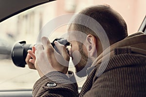 Investigator or private detective or reporter or paparazzi sitting in car and taking photo with professional camera