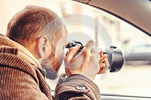 Investigator or private detective or reporter or paparazzi sitting in car and taking photo with professional camera photo