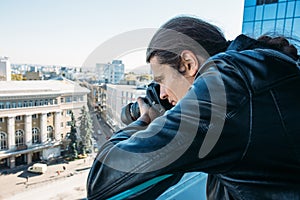 Investigator or private detective or reporter or paparazzi taking photo from balcony of building with professional camera