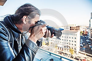 Investigator or private detective or reporter or paparazzi taking photo from balcony of building with professional camera